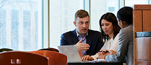 Three business graduate students talking at a table in front of a computer