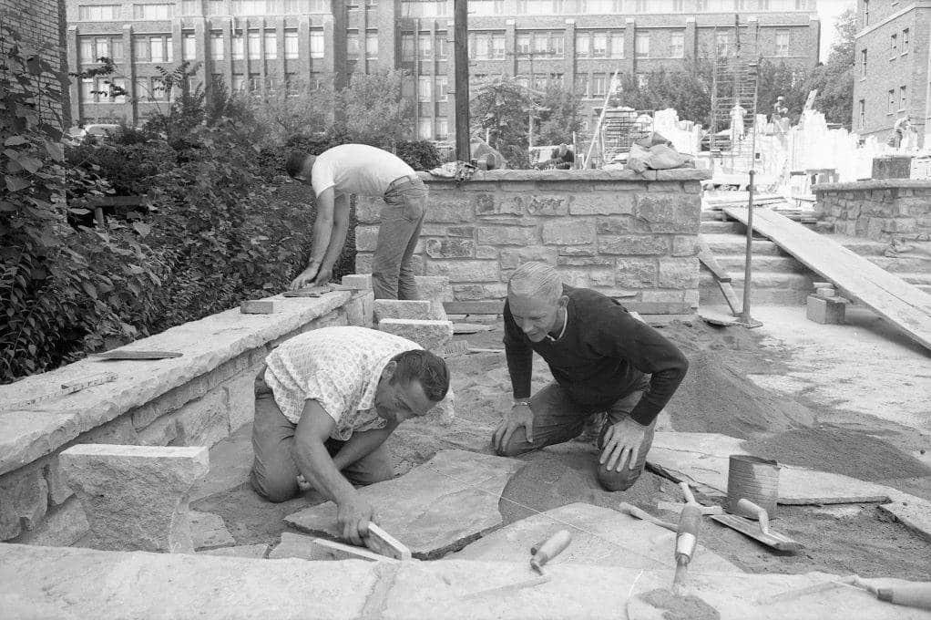 Workers place stone pavers in the plaza to the east of the St. Joan of Arc Chapel.
