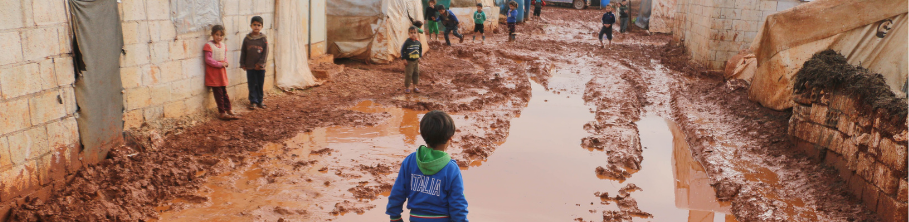 Third world setting. Children standing outside concrete-brick housing and mud-covered tents; ankle-deep in mud.