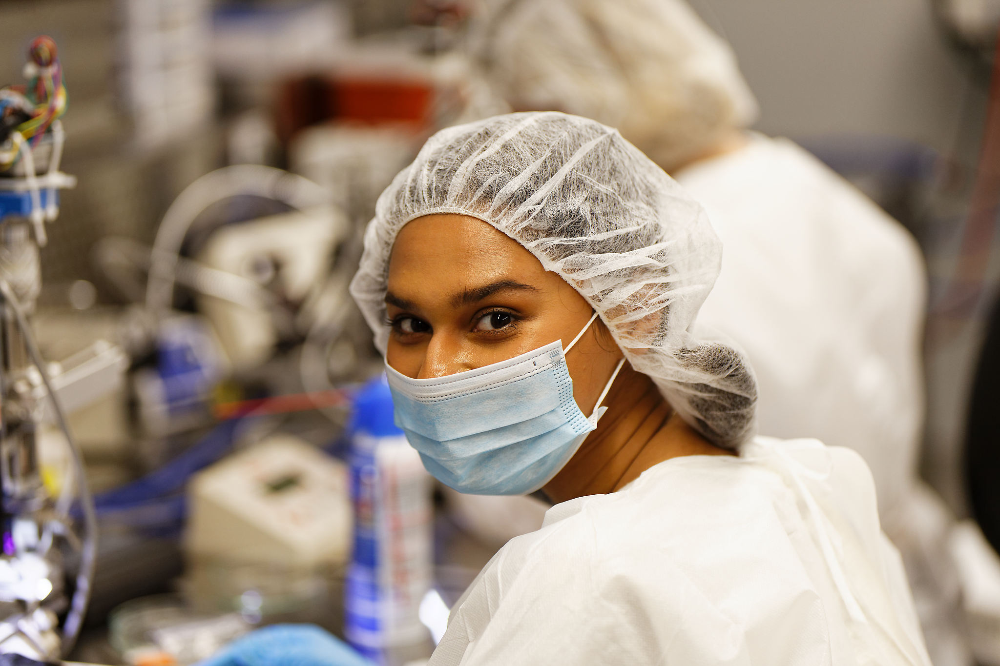 A student wearing a mask and hairnet in a laboratory. 
