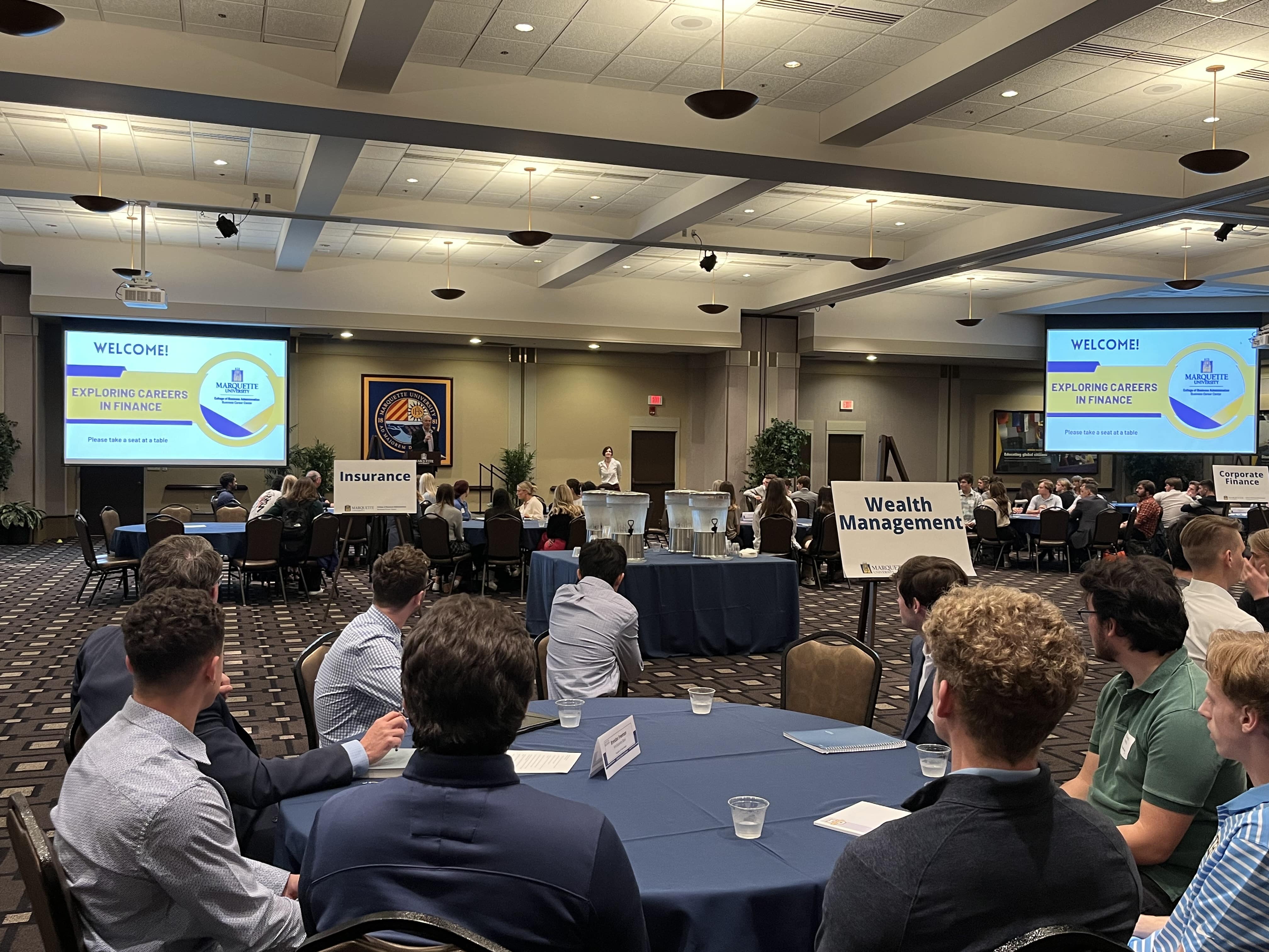 A bunch of people sit at a table watching a presentation.