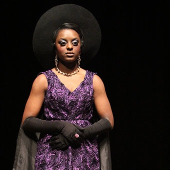 Theatre Arts production of student in purple dress with black hat and gloves