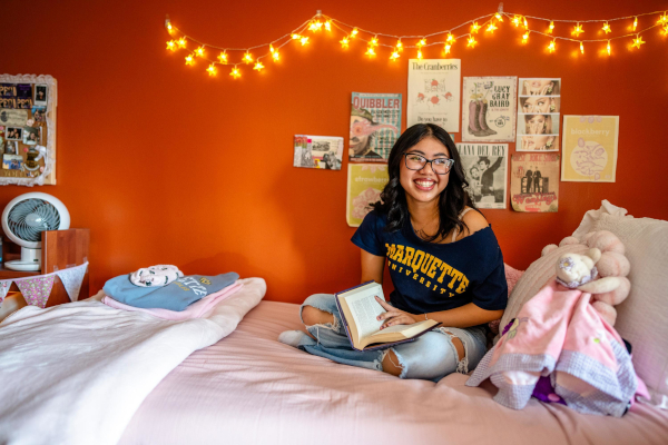 Student sitting on bed in dorm.