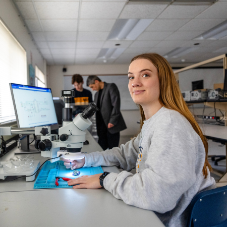 embedded systems undergrad student working in embedded sytems lab with student and faculty in background