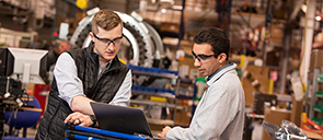 Two men in a warehouse working on a laptop computer.