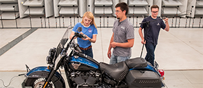 A woman and two men outside working with a motorcycle.