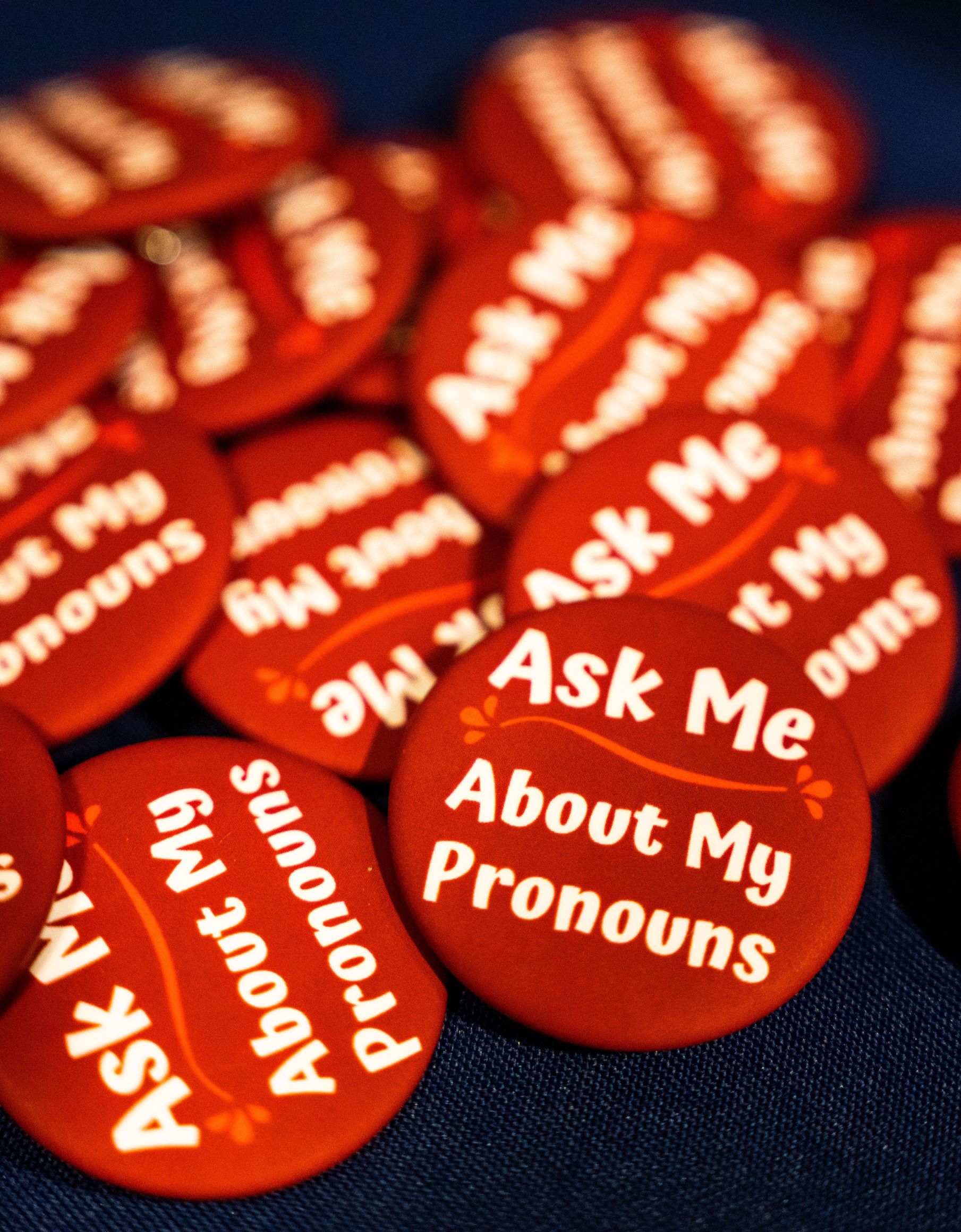 A picture of red pins with white text saying 'ask me about my pronouns'