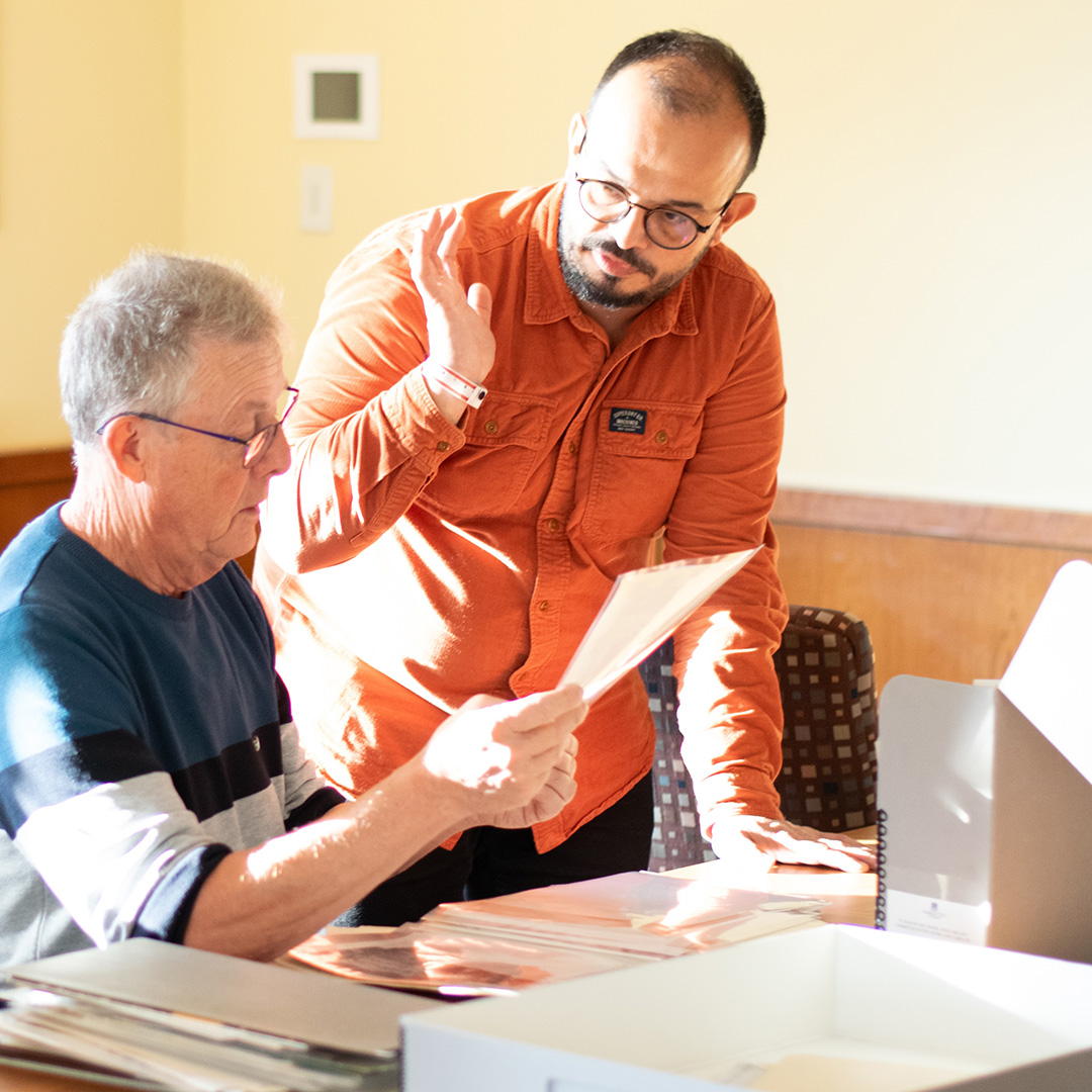 two men seated at archives table looking through photographs of joan of arc chapel