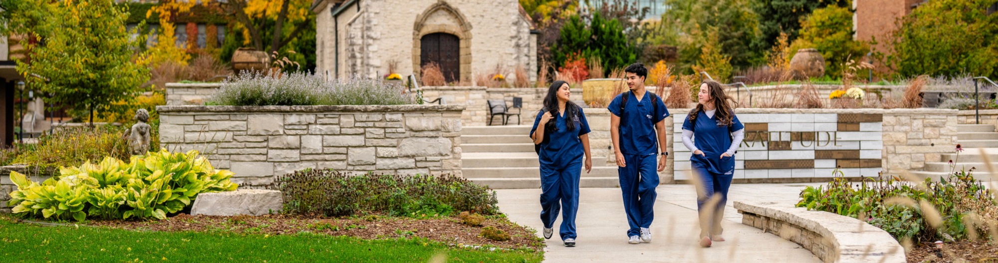 Three students in scrubs walking in front of St. Joan of Arc Chapel.