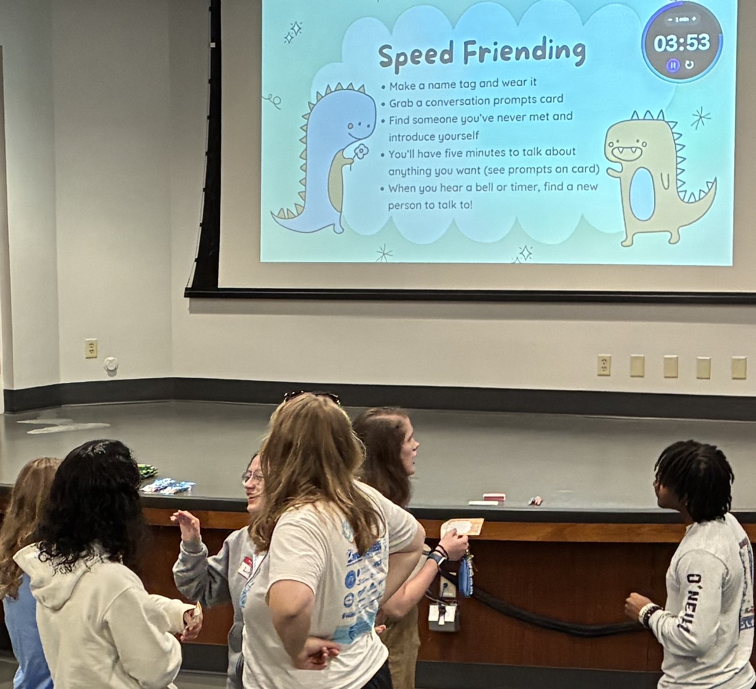 a group of students talking in pairs in front of a projected powerpoint